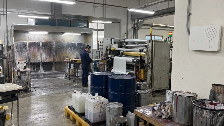 A finishing shop with a spray booth, a coating line and solvent drums, and an air sensor on a wall away from the booth