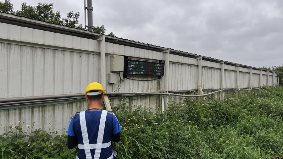 A worker in a hard hat by a site hoarding fitted with sensor boxes and an LED display board